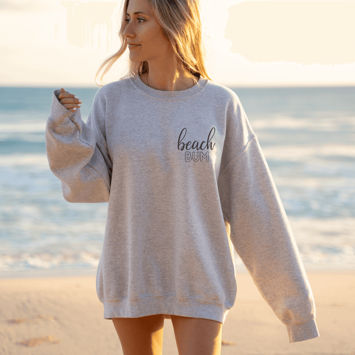 Woman wearing Beach Bum ash grey crewneck sweatshirt on a sunny beach.