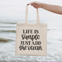 Hand holding Life is Simple Canvas Tote Bag with ocean background, organic cotton tote for carrying essentials, stylish and durable