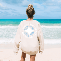 Woman wearing Save the Manta Rays Sand Crewneck Sweatshirt on beach, showcasing ocean conservation message.