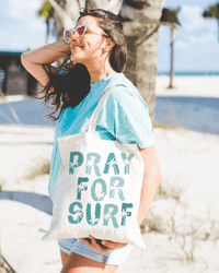 Woman with Pray for Surf Canvas Tote Bag at the beach, perfect for holding beach essentials.