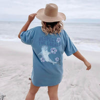 Woman on beach wearing Whale Shark Respect the Locals Blue Graphic Tee with ocean and conservation theme.