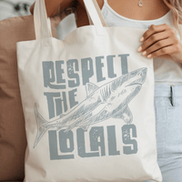 Woman holding Respect the Locals Shark Canvas Tote Bag supporting shark conservation, 100% organic cotton, 15x16in size, twin carry handles.