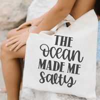 Person holding The Ocean Made Me Salty Canvas Tote Bag made of 100% organic cotton with twin carry handles.